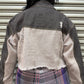 Person wearing a denim jacket and plaid pants standing in front of a metal shutter.