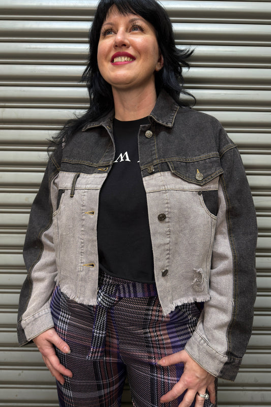 Woman wearing a denim jacket and plaid pants standing in front of a metal shutter.