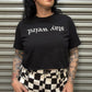 Person wearing a black t-shirt with 'stay weird' text in front of a metallic shutter.