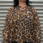 Woman wearing a leopard print blouse standing in front of a metallic shutter.