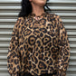 Woman wearing a leopard print blouse standing in front of a metal shutter.