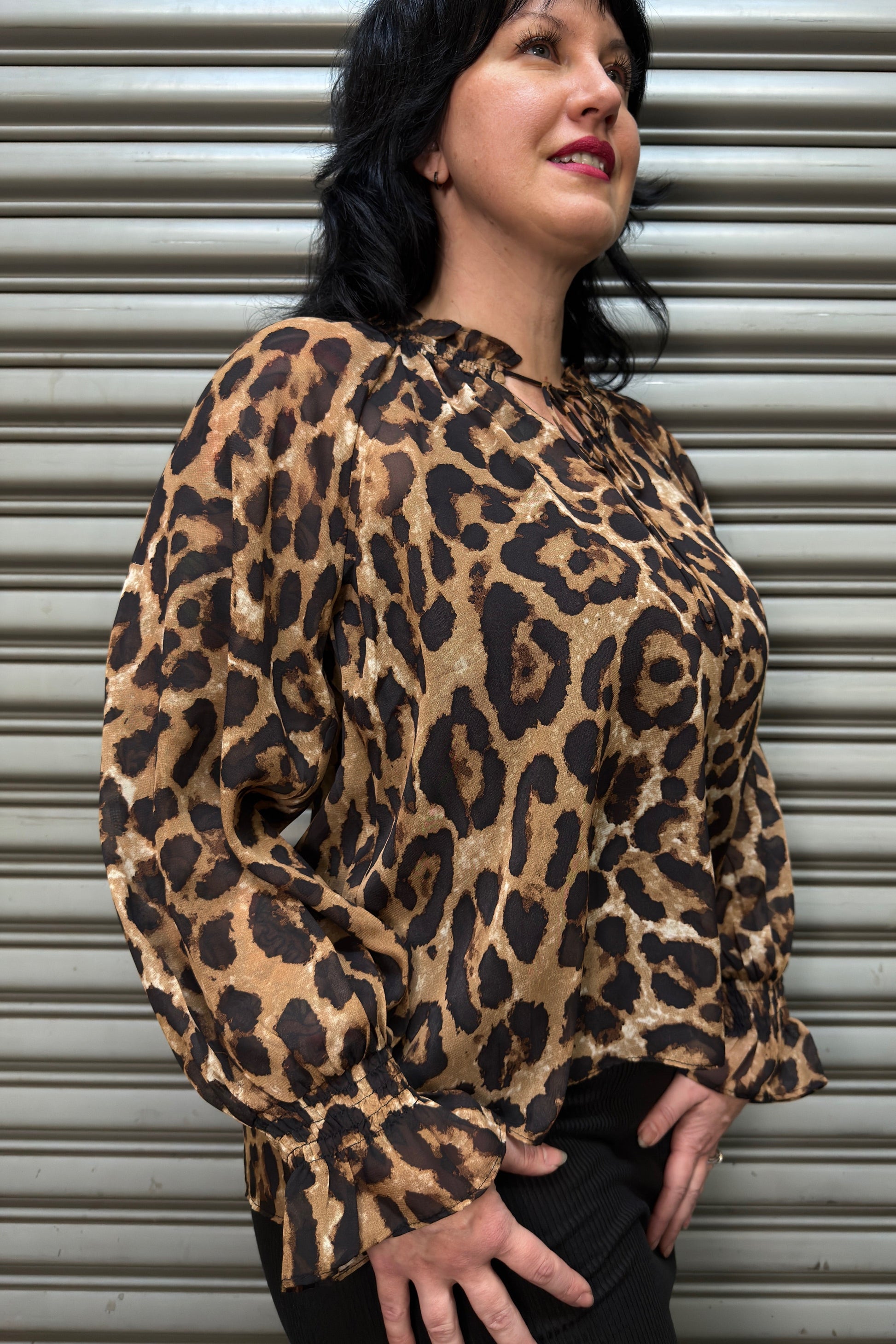 Woman wearing a leopard print blouse standing against a metallic shutter.