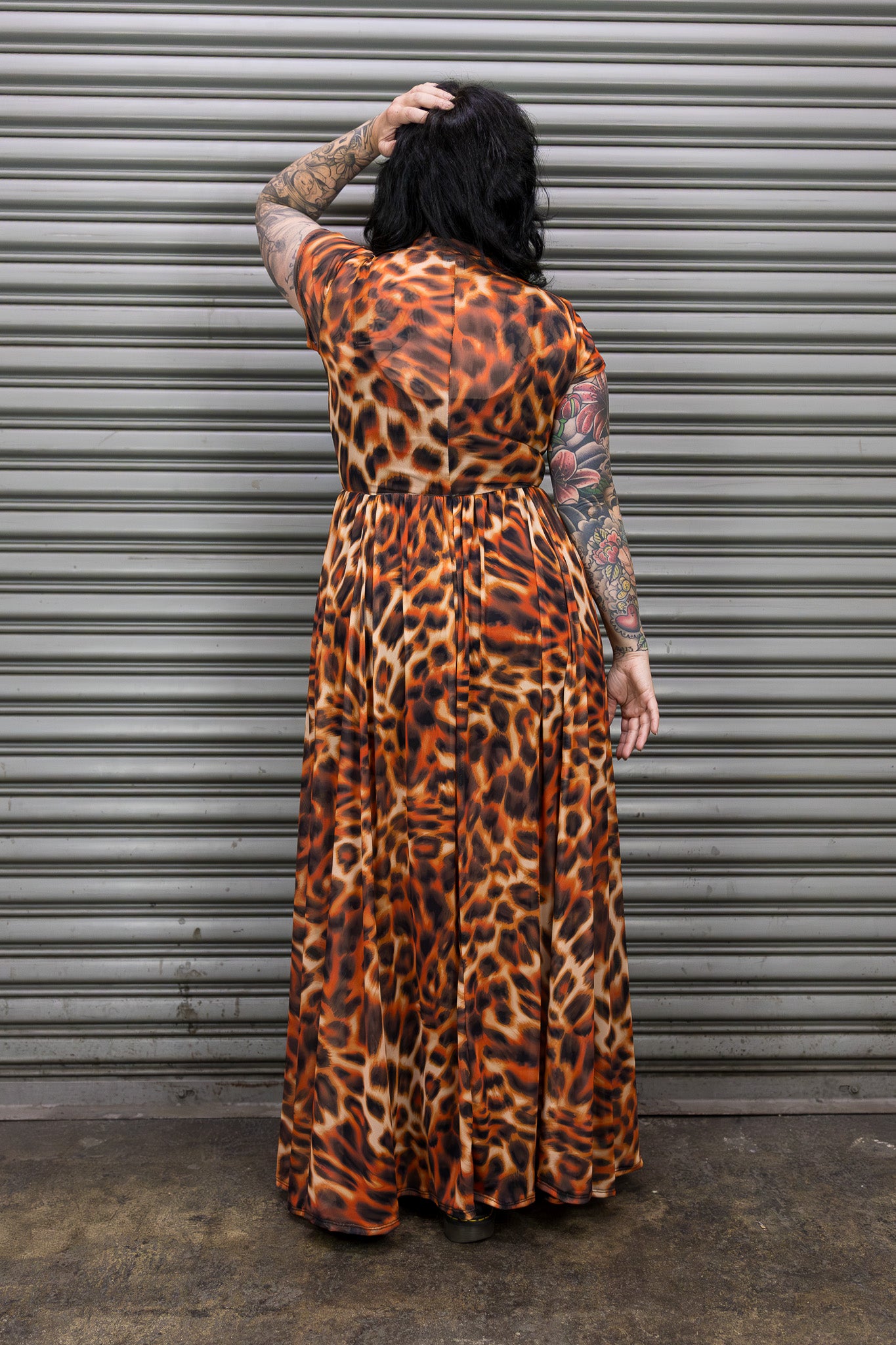 Person wearing a leopard print dress standing in front of a metal shutter.