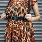 Person wearing a leopard print dress with a black belt against a metallic background