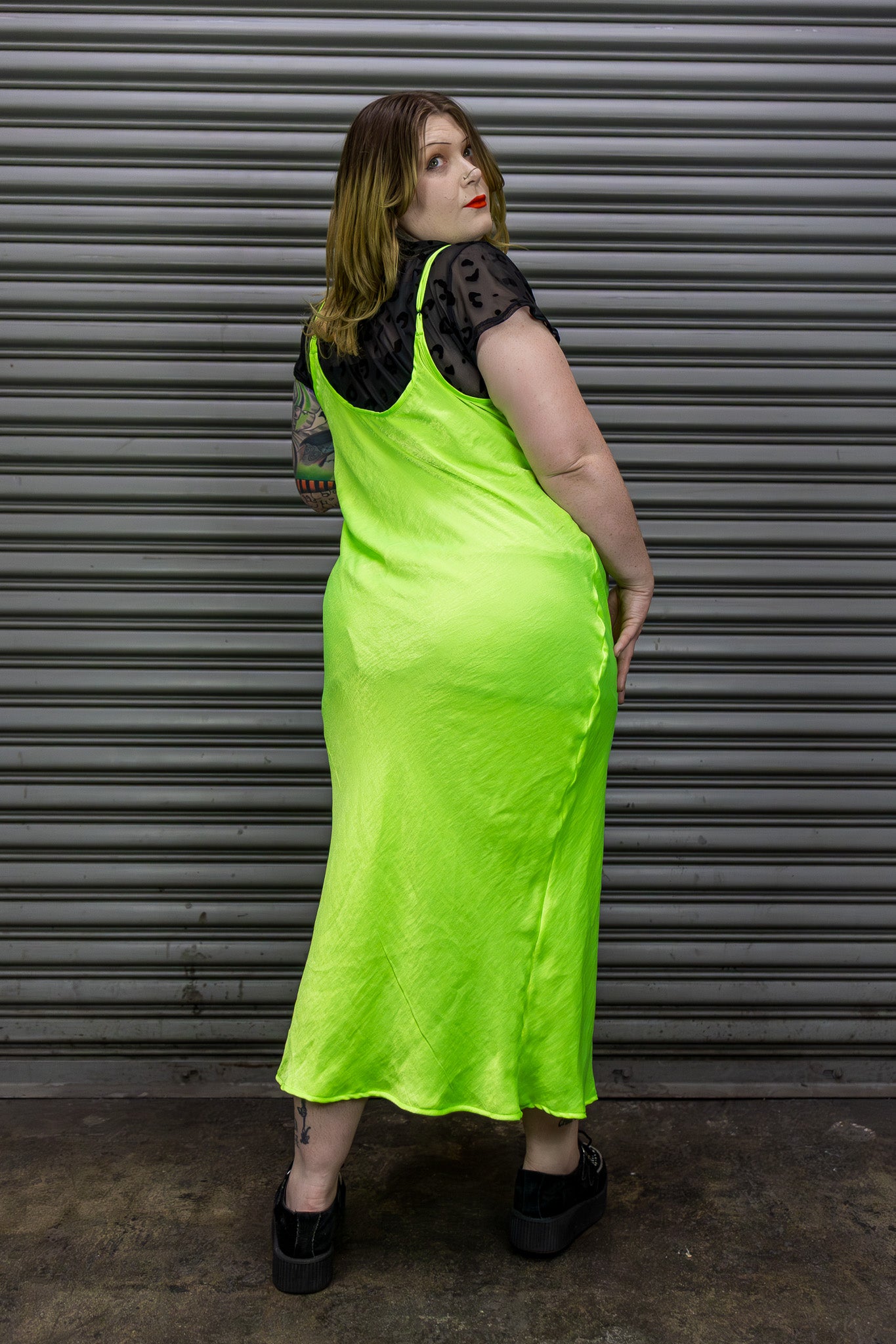 Woman wearing a bright green slip dress with black lace details against a metal shutter background.