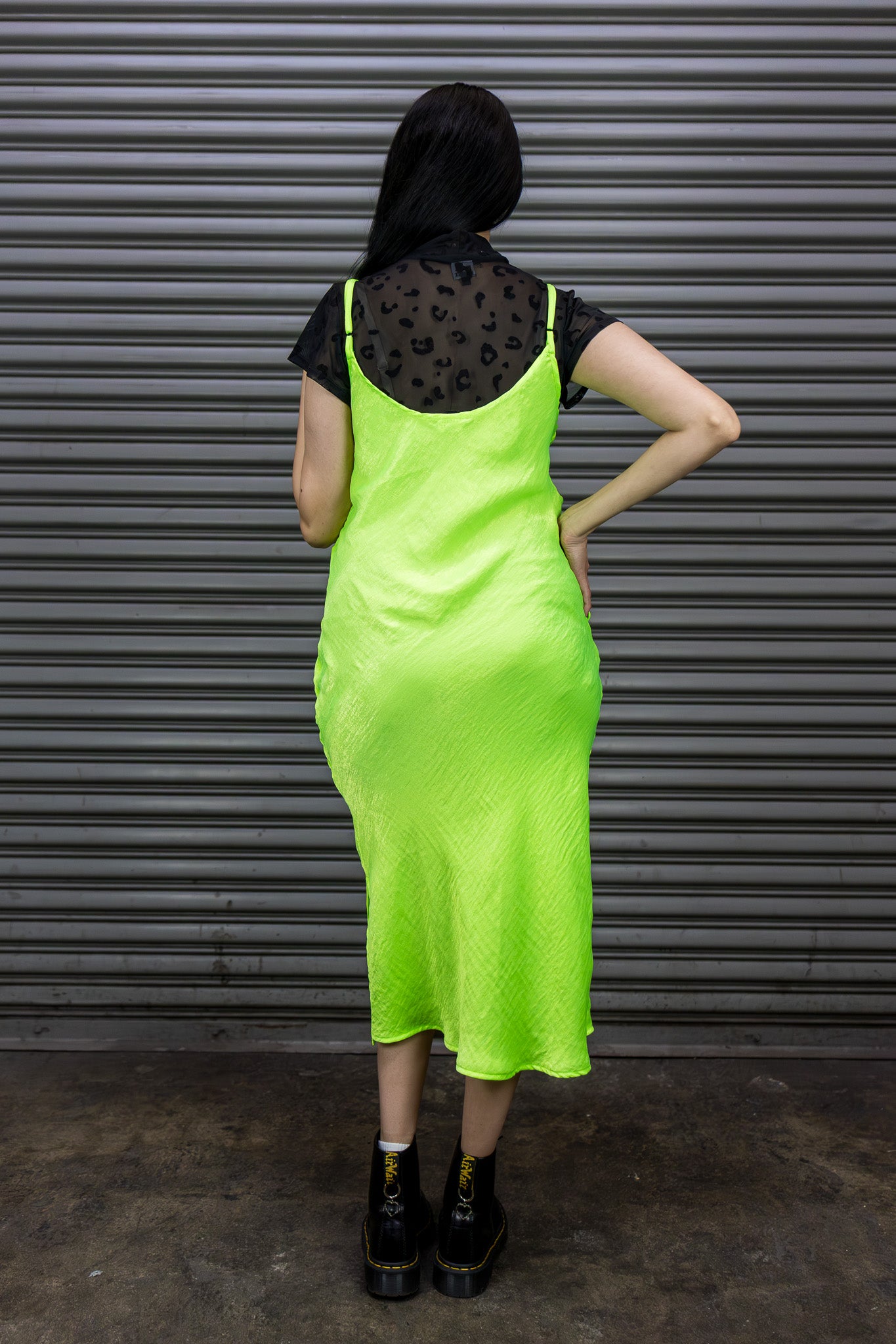 Person wearing a bright green slip dress with a black leopard print top against a metallic shutter background.