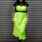 Person wearing a bright green dress with a black leather harness against a metal shutter background