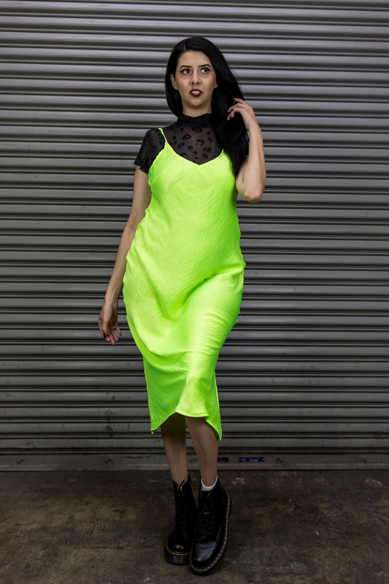 Woman wearing a bright green dress with black sleeves against a metallic shutter background