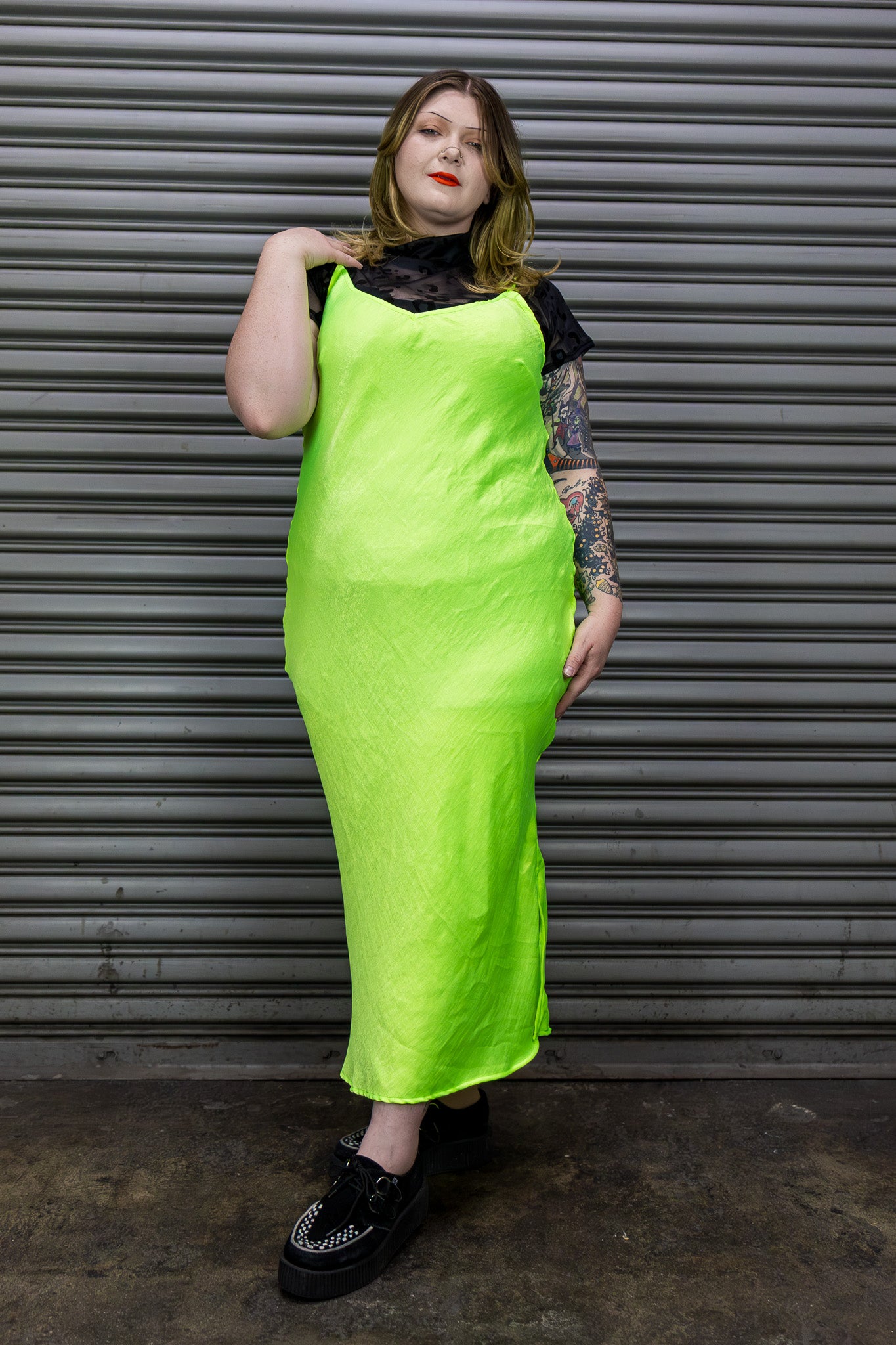 Person wearing a bright green dress with black lace top against a metallic shutter background