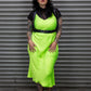 Person wearing a bright green dress and leather harness standing in front of a metal shutter.