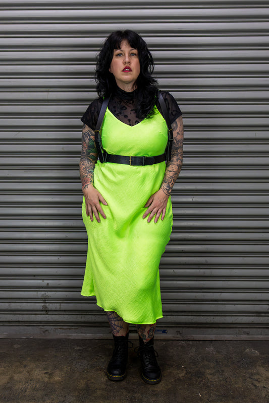 Person wearing a bright green dress and leather harness standing in front of a metal shutter.