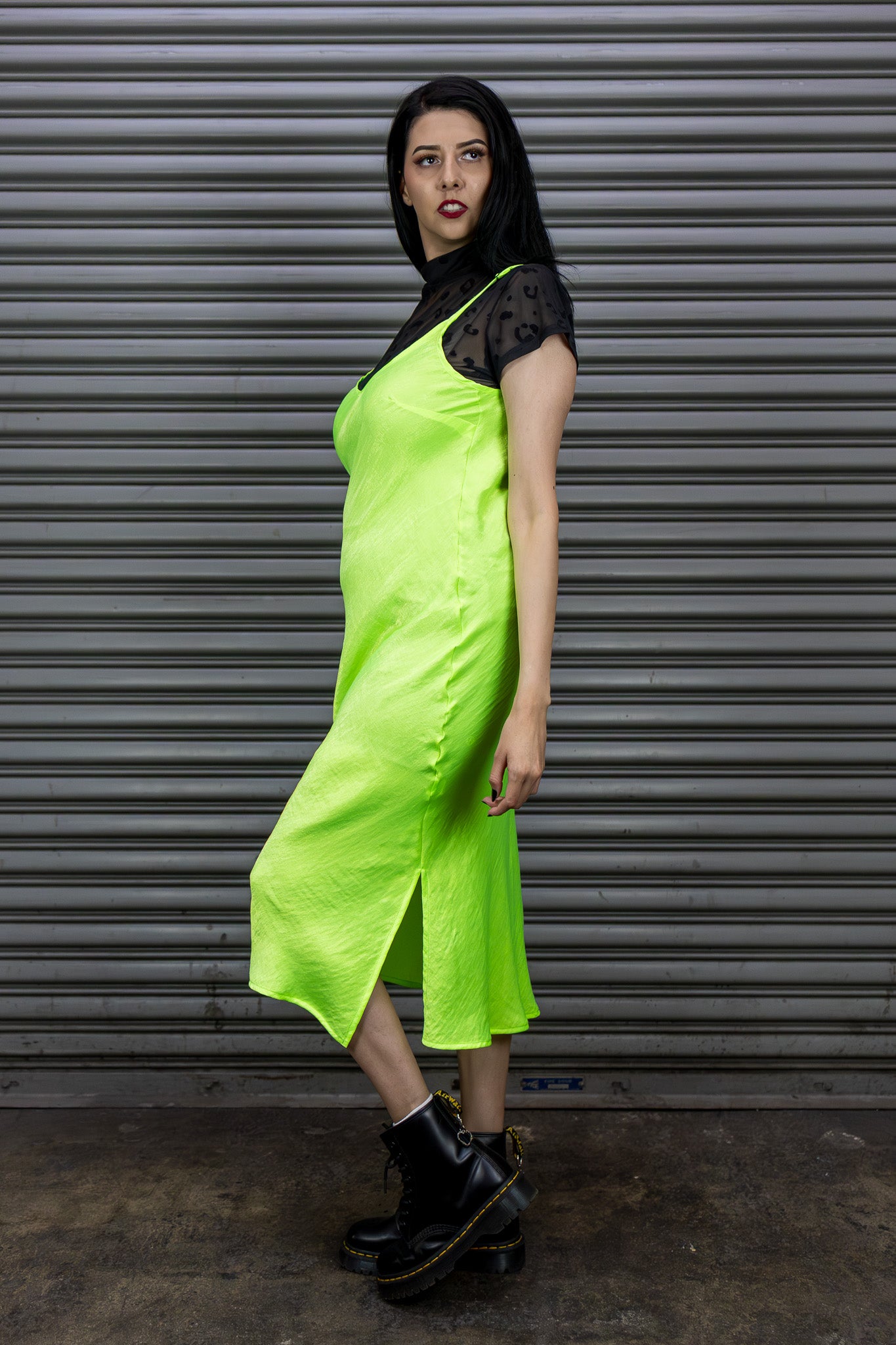 Person wearing a bright green dress with black lace details against a metallic shutter background