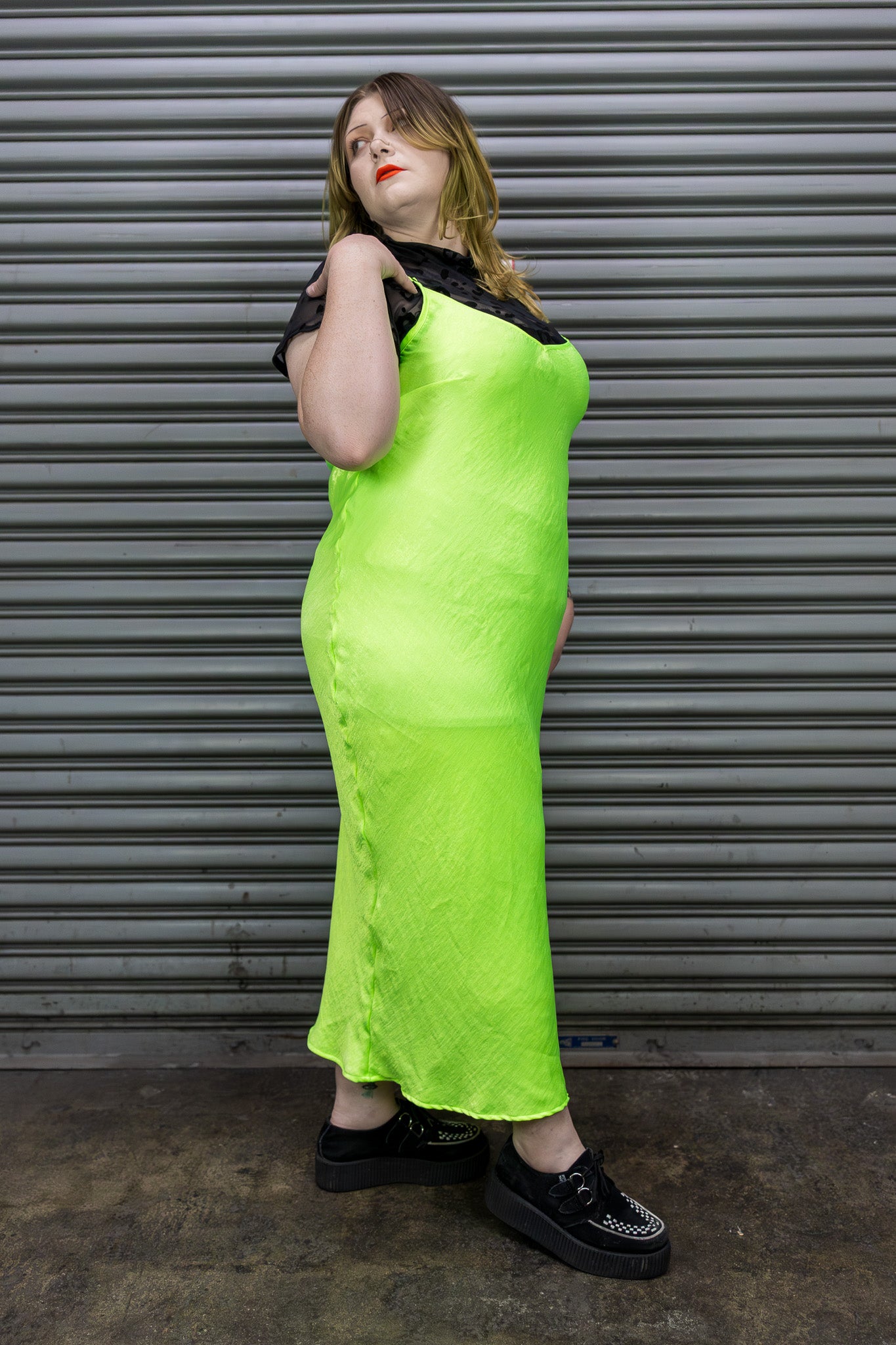 Person wearing a bright green dress standing in front of a metallic shutter.