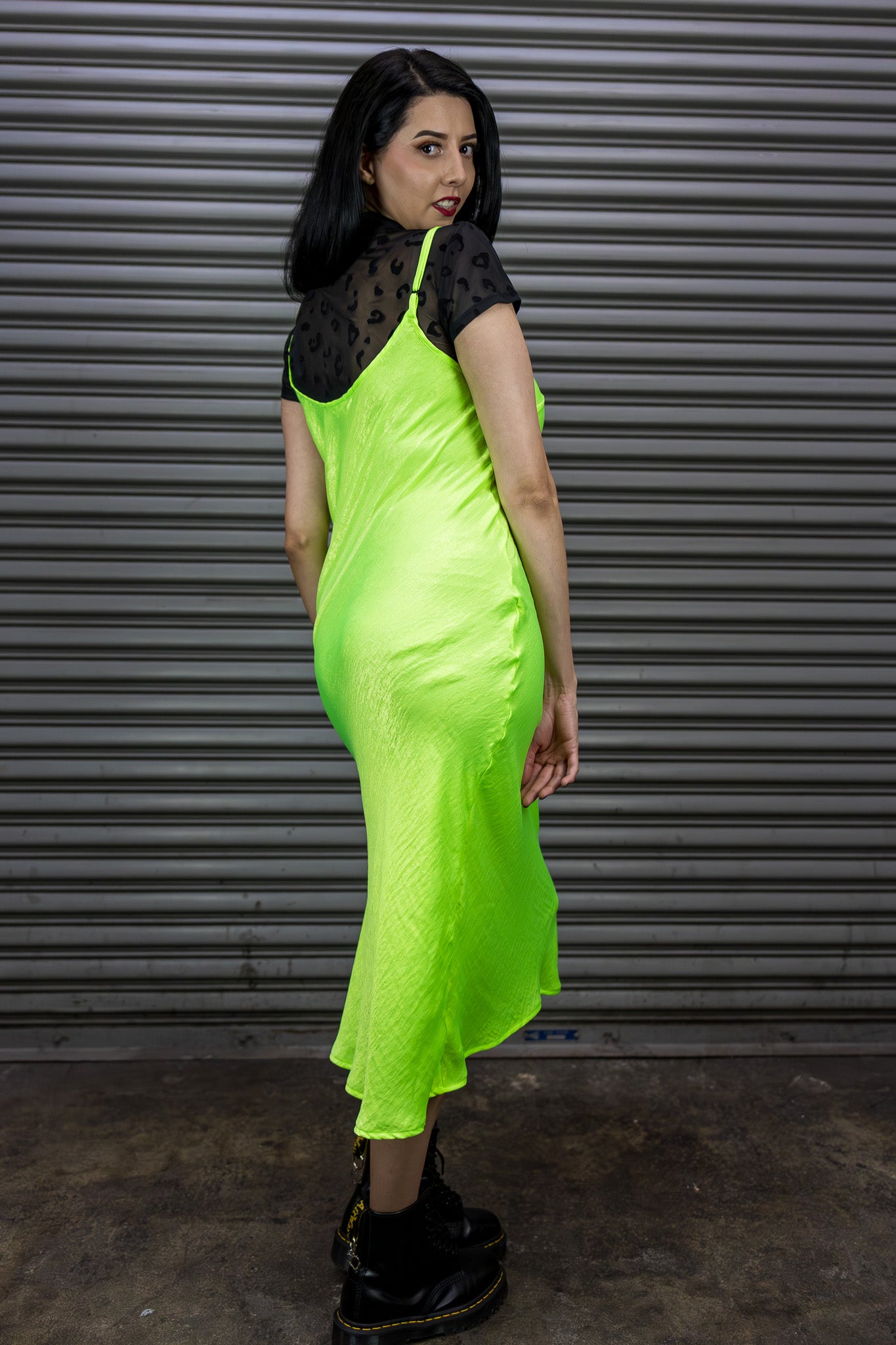 Woman wearing a neon green dress with black accents against a metallic shutter background.