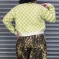 Person wearing a green and white checkered sweater and leopard print pants against a metallic shutter background.