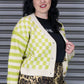 Woman wearing a green and white checkered cardigan over a black top with leopard print pants, standing against a metallic shutter.