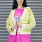 Woman wearing a green and white checkered cardigan over a pink t-shirt with a graphic design, standing in front of a metallic shutter.