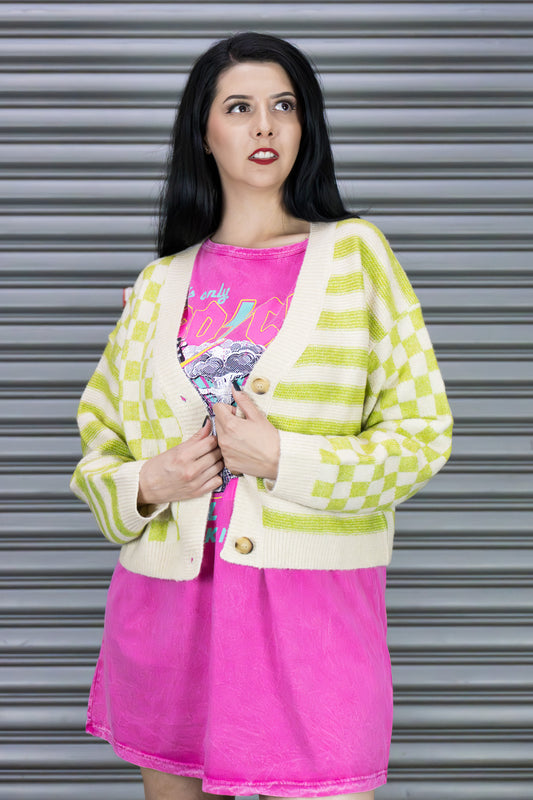 Woman wearing a green and white checkered cardigan over a pink t-shirt with a graphic design, standing in front of a metallic shutter.