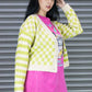 Woman wearing a bright yellow and white checkered cardigan over a pink t-shirt with graphic design, standing against a metallic shutter.