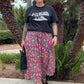 Person wearing a black t-shirt and pink floral skirt standing in front of palm trees.