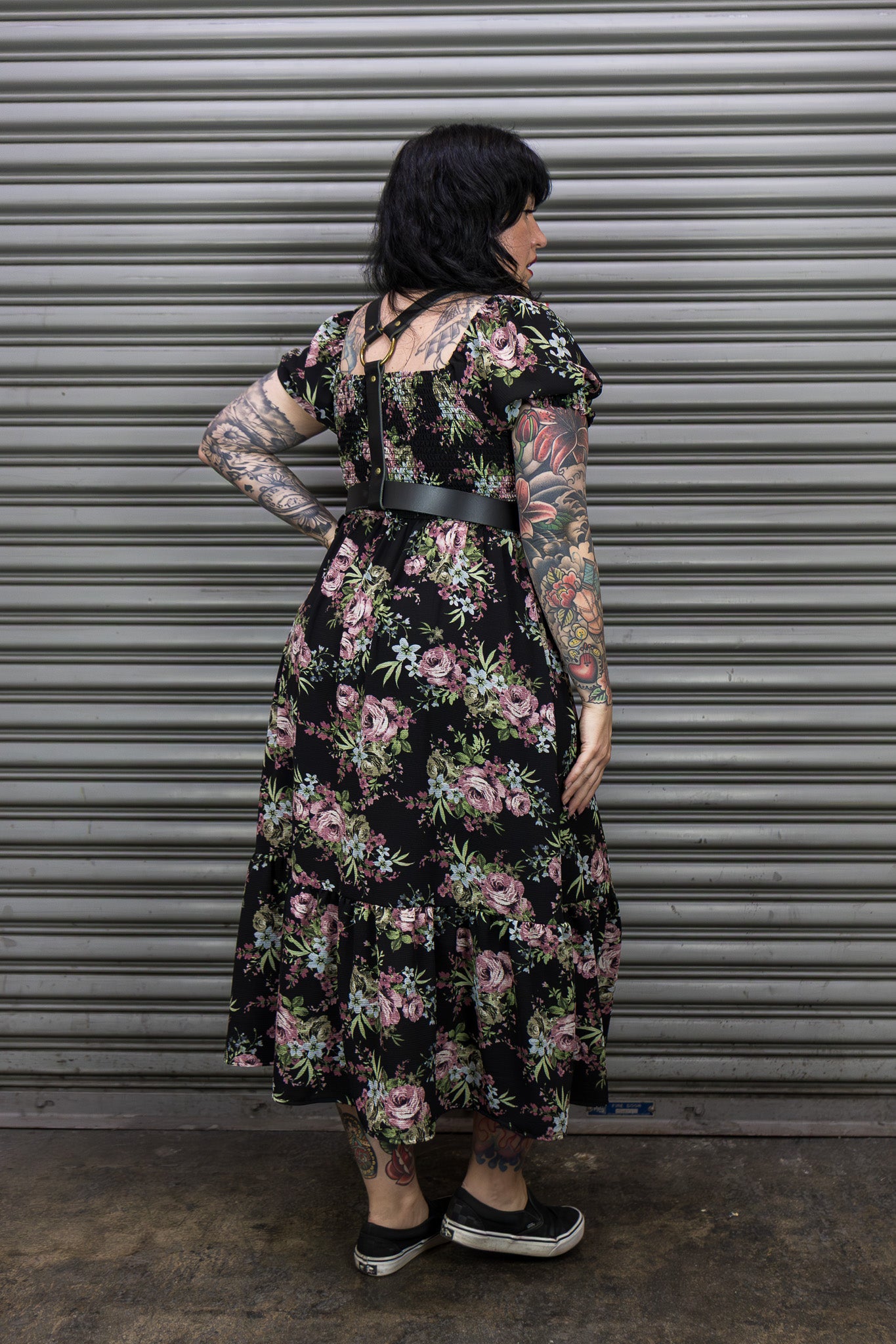 Person wearing a floral dress standing in front of a metallic shutter.