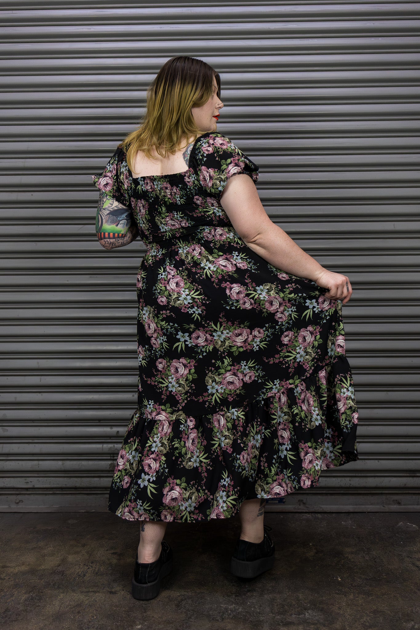 Woman wearing a floral dress standing against a metallic shutter.
