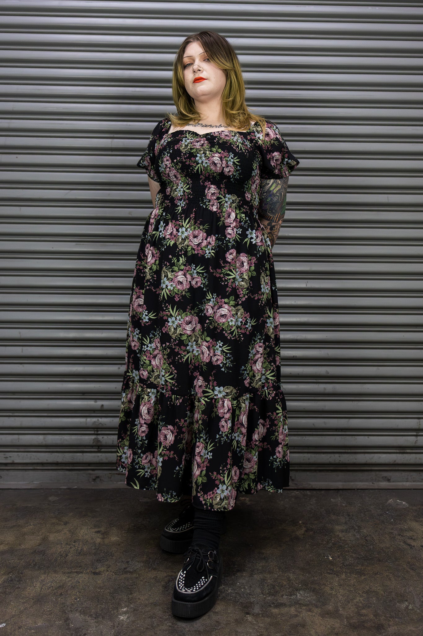 Person wearing a floral dress standing in front of a metal shutter.