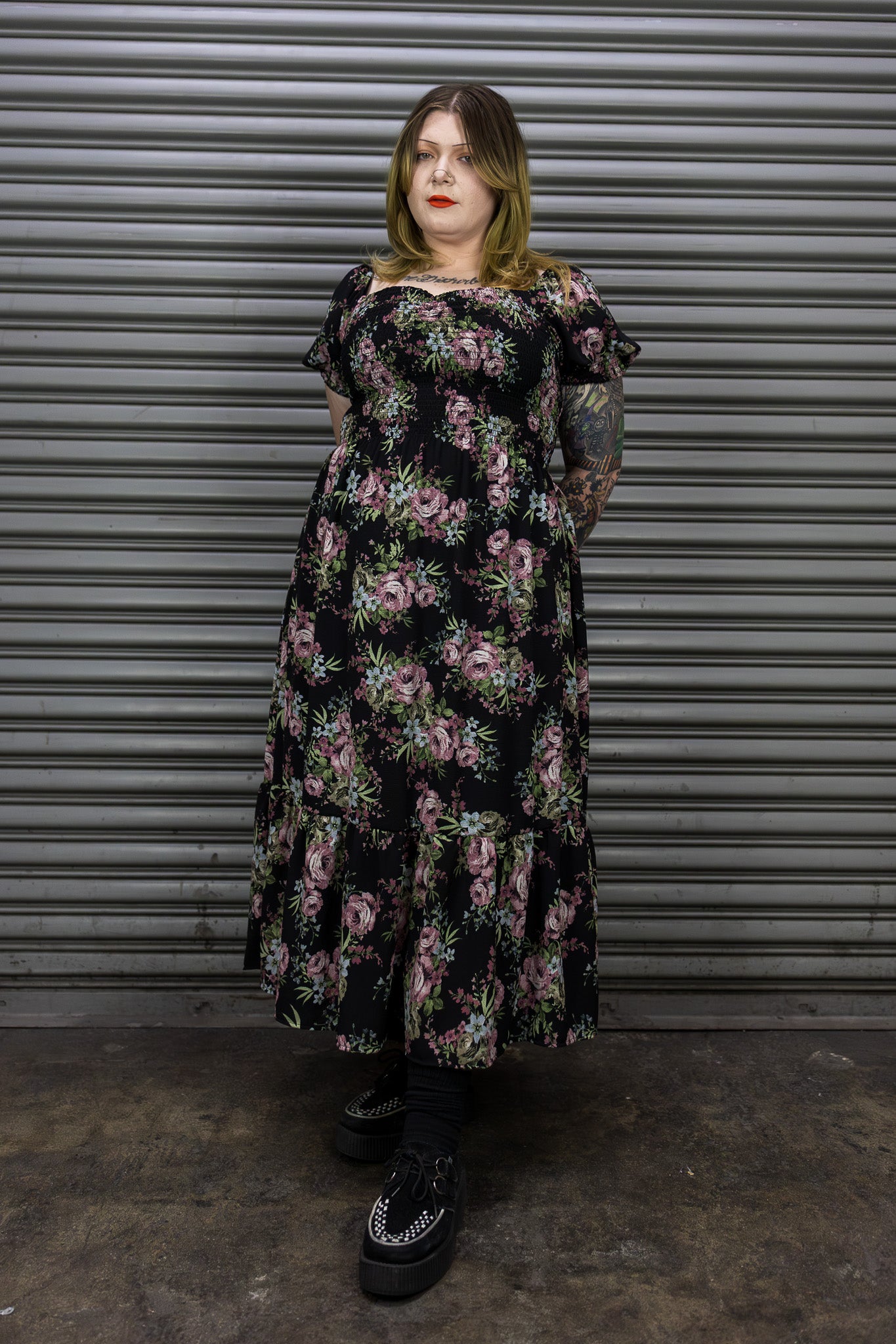 Person wearing a floral dress standing in front of a metallic shutter.