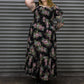 Woman wearing a floral dress standing in front of a corrugated metal wall.
