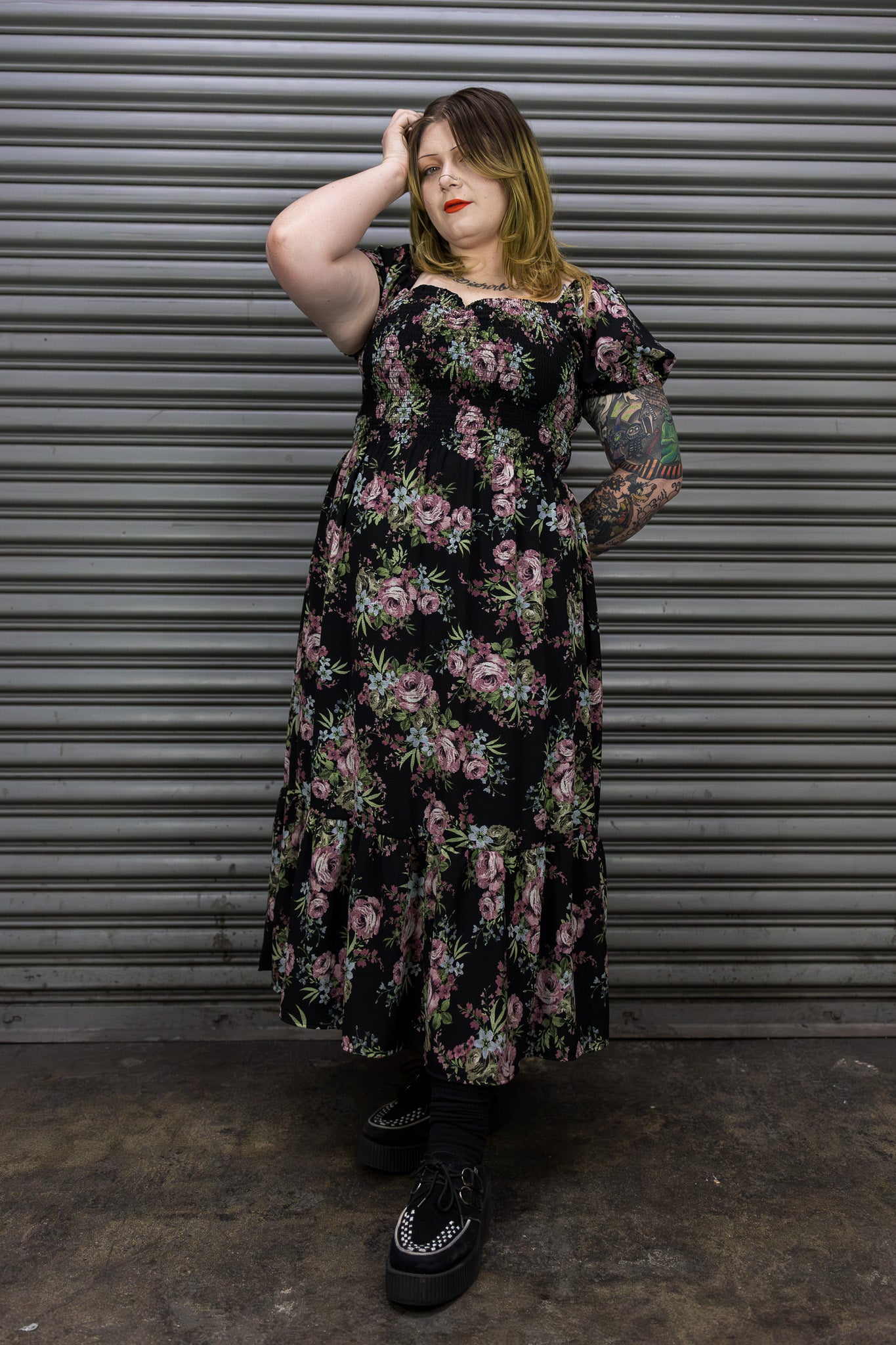 Woman wearing a floral dress standing in front of a corrugated metal wall.