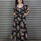 Woman wearing a floral dress standing in front of a metal shutter.