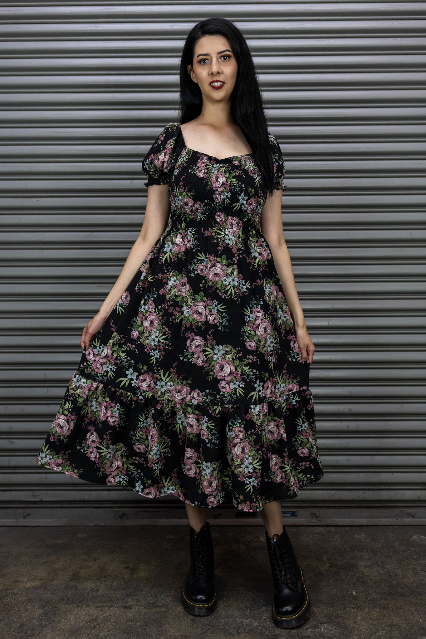 Woman wearing a floral dress standing in front of a metal shutter.