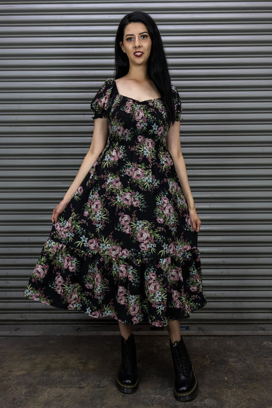 Woman wearing a floral dress standing in front of a metal shutter.