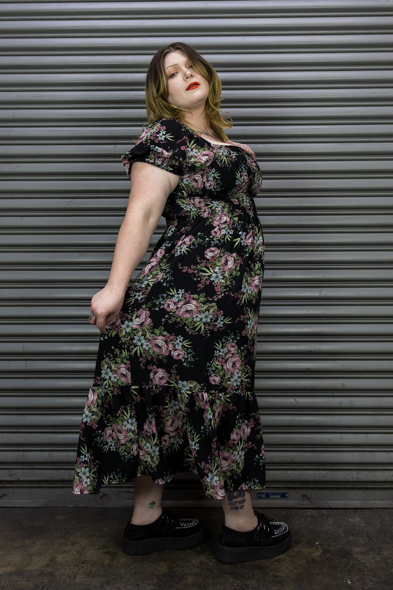 Woman wearing a floral dress standing in front of a metal shutter.