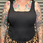 Person wearing a black tank top and leopard print skirt with tattoos on arms and neck.