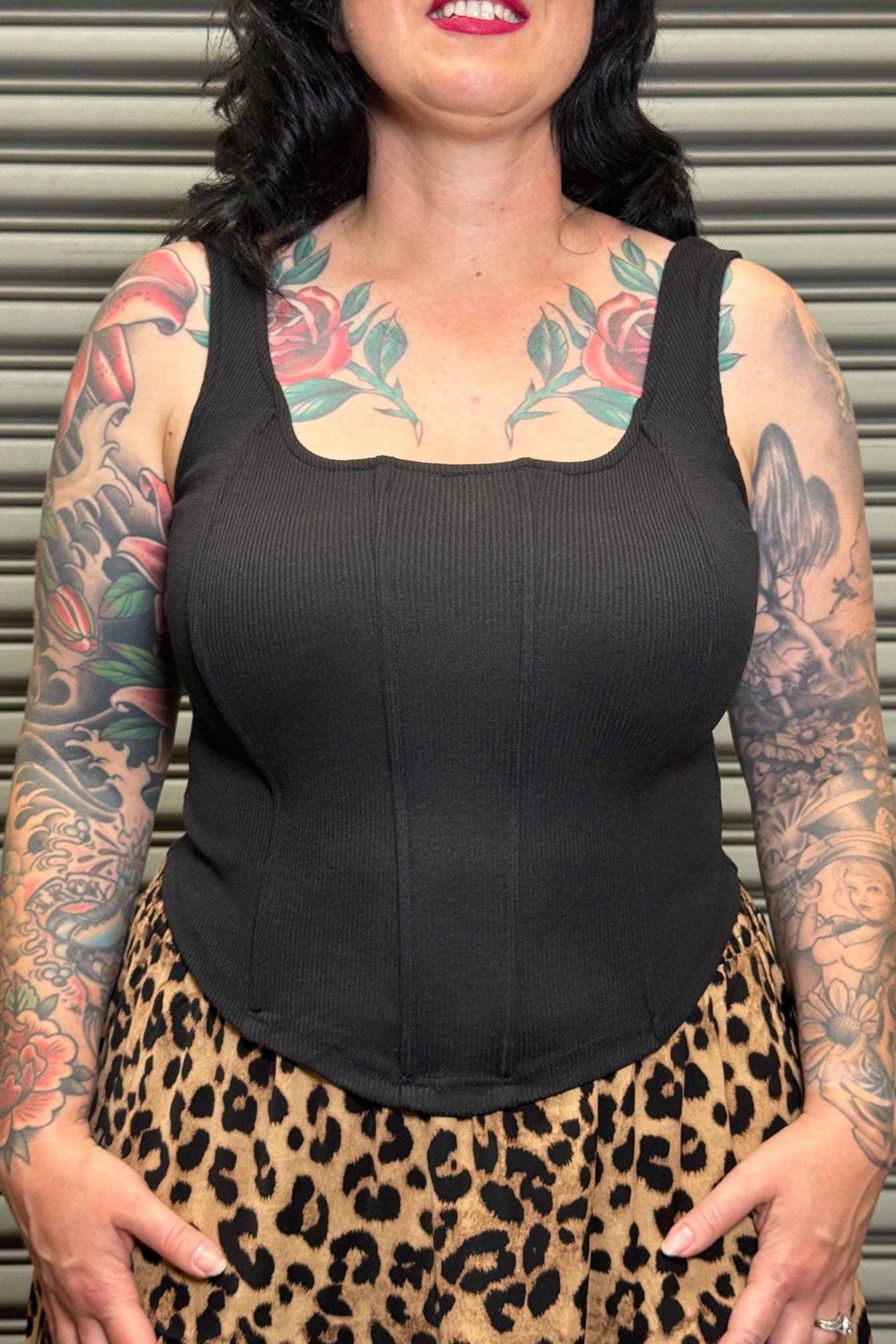 Person wearing a black tank top and leopard print skirt with tattoos on arms and neck.