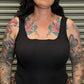 Woman wearing a black tank top and leopard print pants with tattoos on her arms and neck.