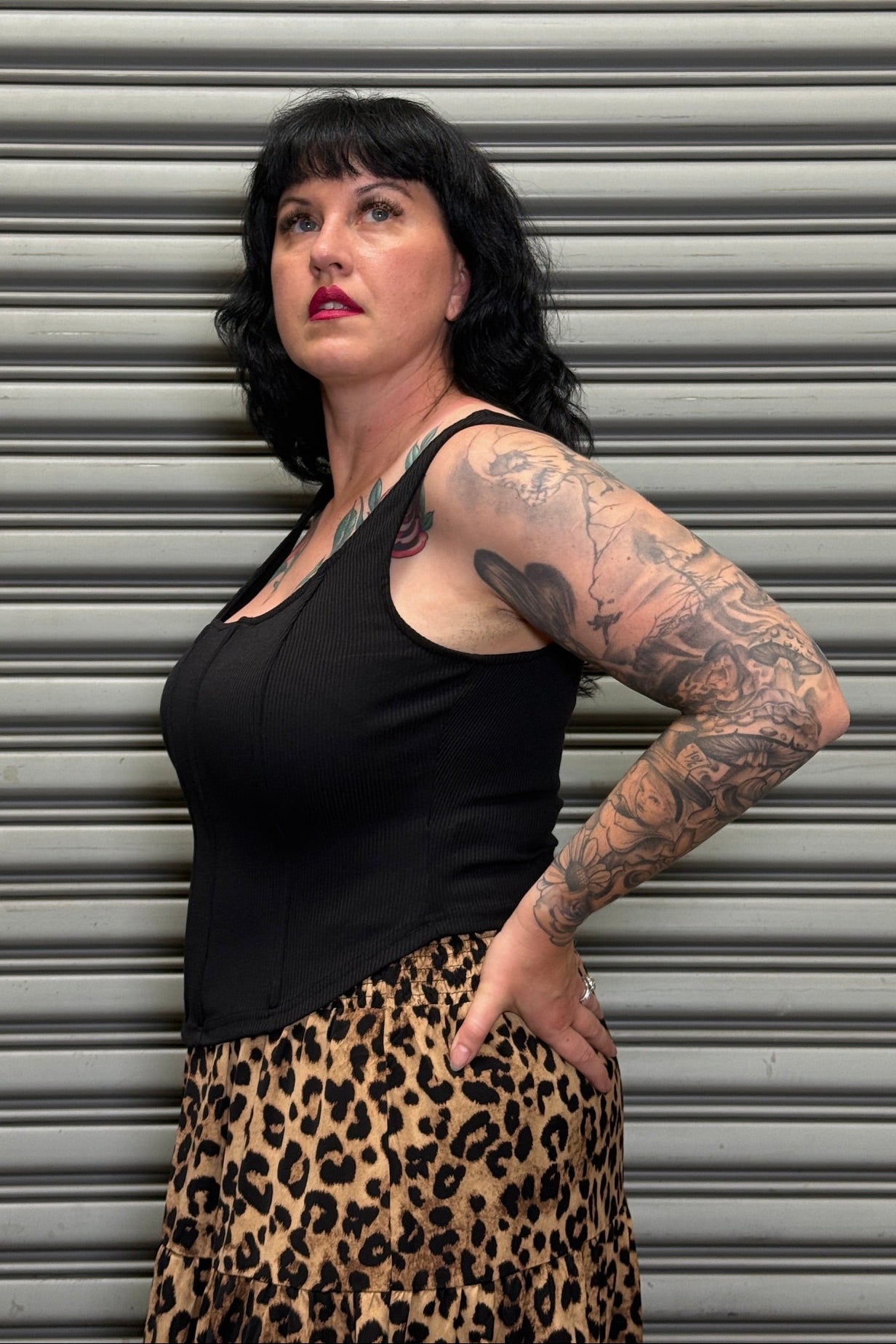 Woman wearing a black tank top and leopard print skirt standing against a metallic shutter.