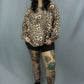 A woman modeling a leopard print long-sleeve top, black shorts, and black lace-up shoes against a gray studio backdrop.