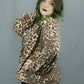 A person modeling a leopard-print long-sleeve top and black wide-leg pants with decorative eyelets down the side, standing against a plain gray backdrop.