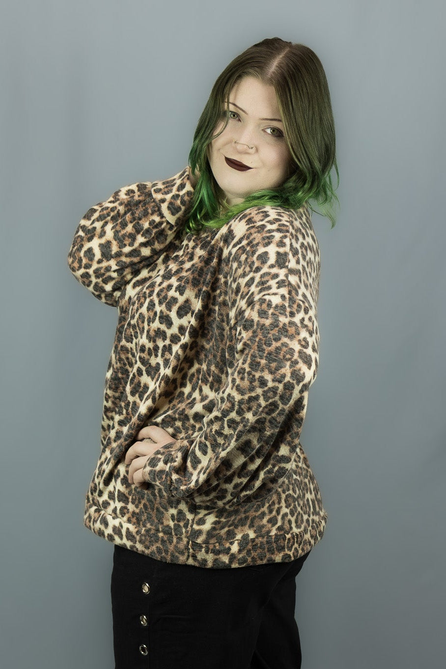 A person modeling a leopard-print long-sleeve top and black wide-leg pants with decorative eyelets down the side, standing against a plain gray backdrop.
