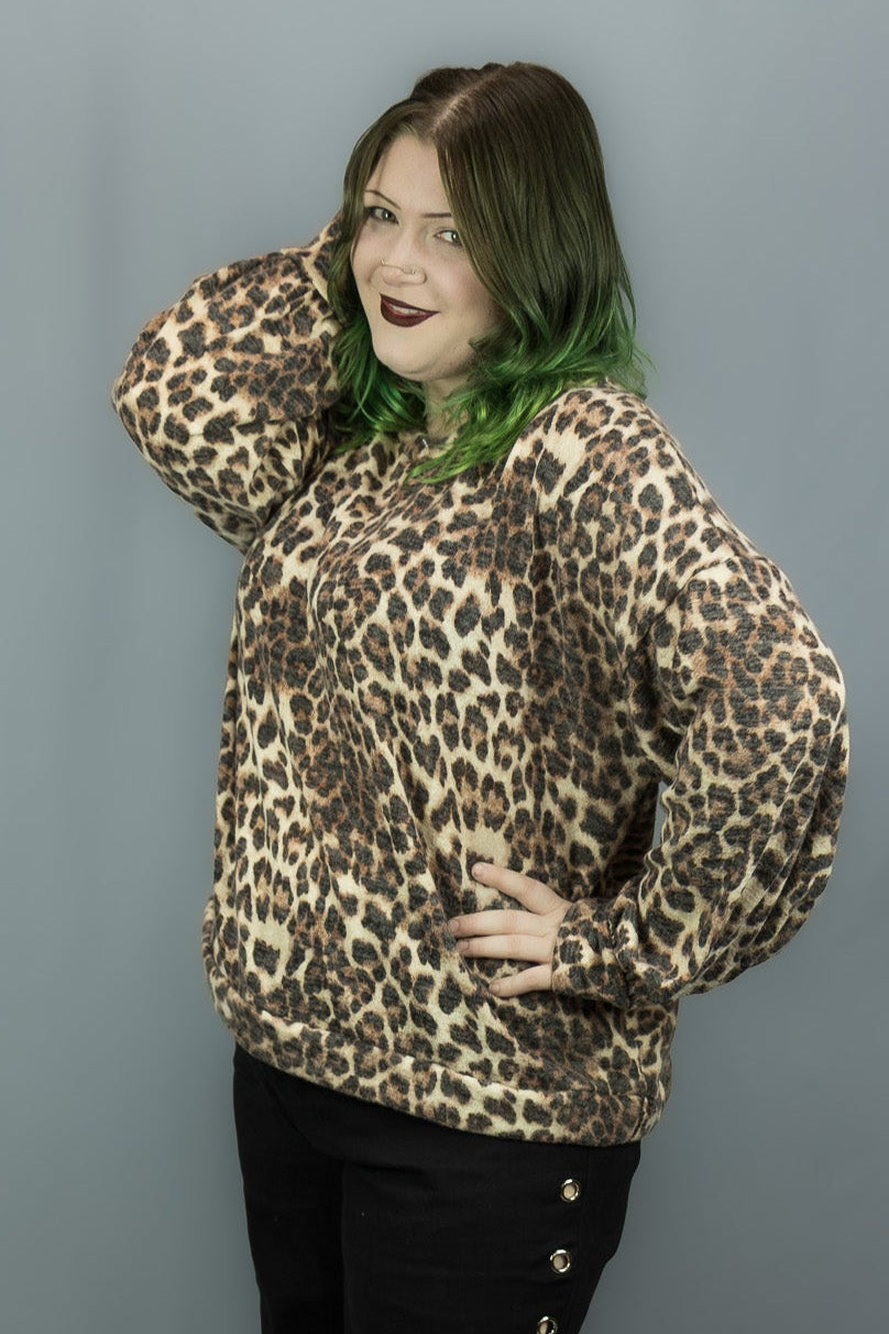 A woman modeling a leopard print long-sleeve sweater and black pants with side grommets, standing against a gray studio backdrop.