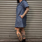 Person wearing a blue leopard print denim dress and black boots standing against a corrugated metal wall.