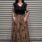 Woman wearing a black top and leopard print skirt standing in front of a metal shutter.