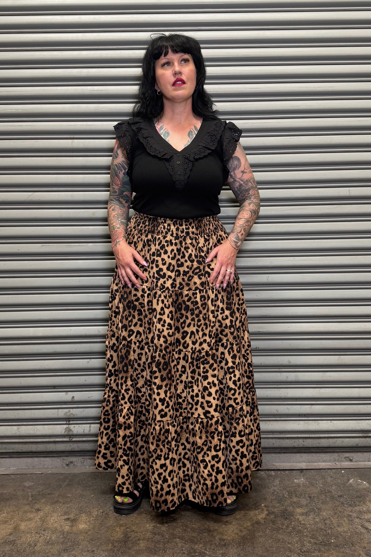 Woman wearing a black top and leopard print skirt standing in front of a metal shutter.