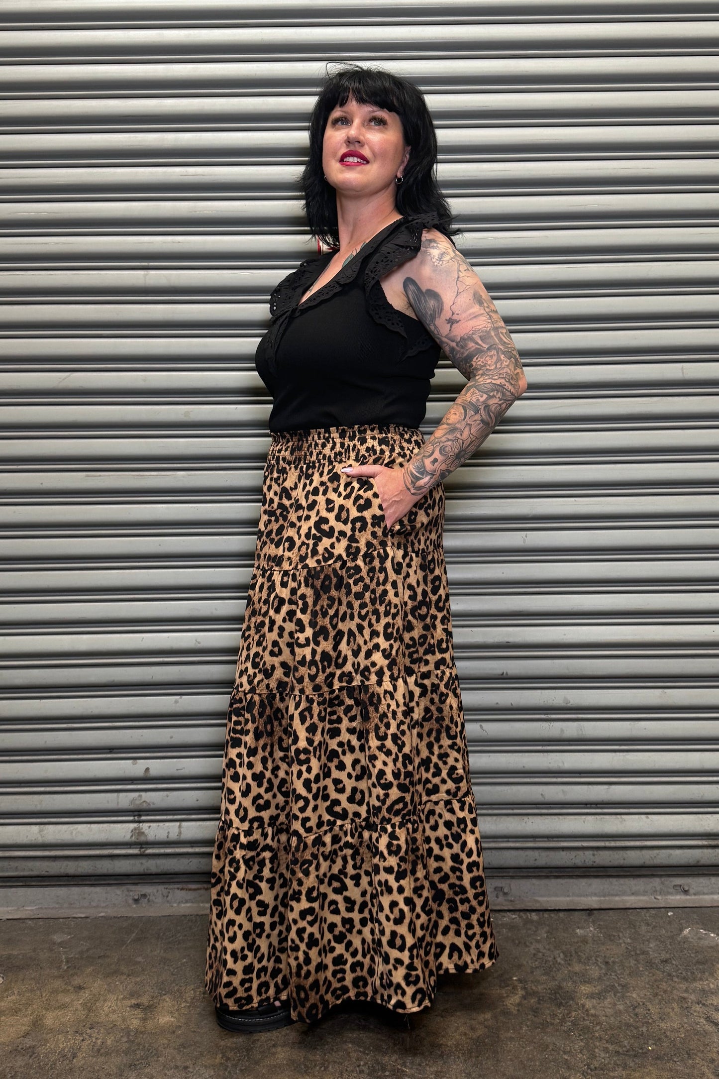 Side view of the Wild Heart leopard print tiered maxi skirt with pockets paired with a black ruffle sleeve top.