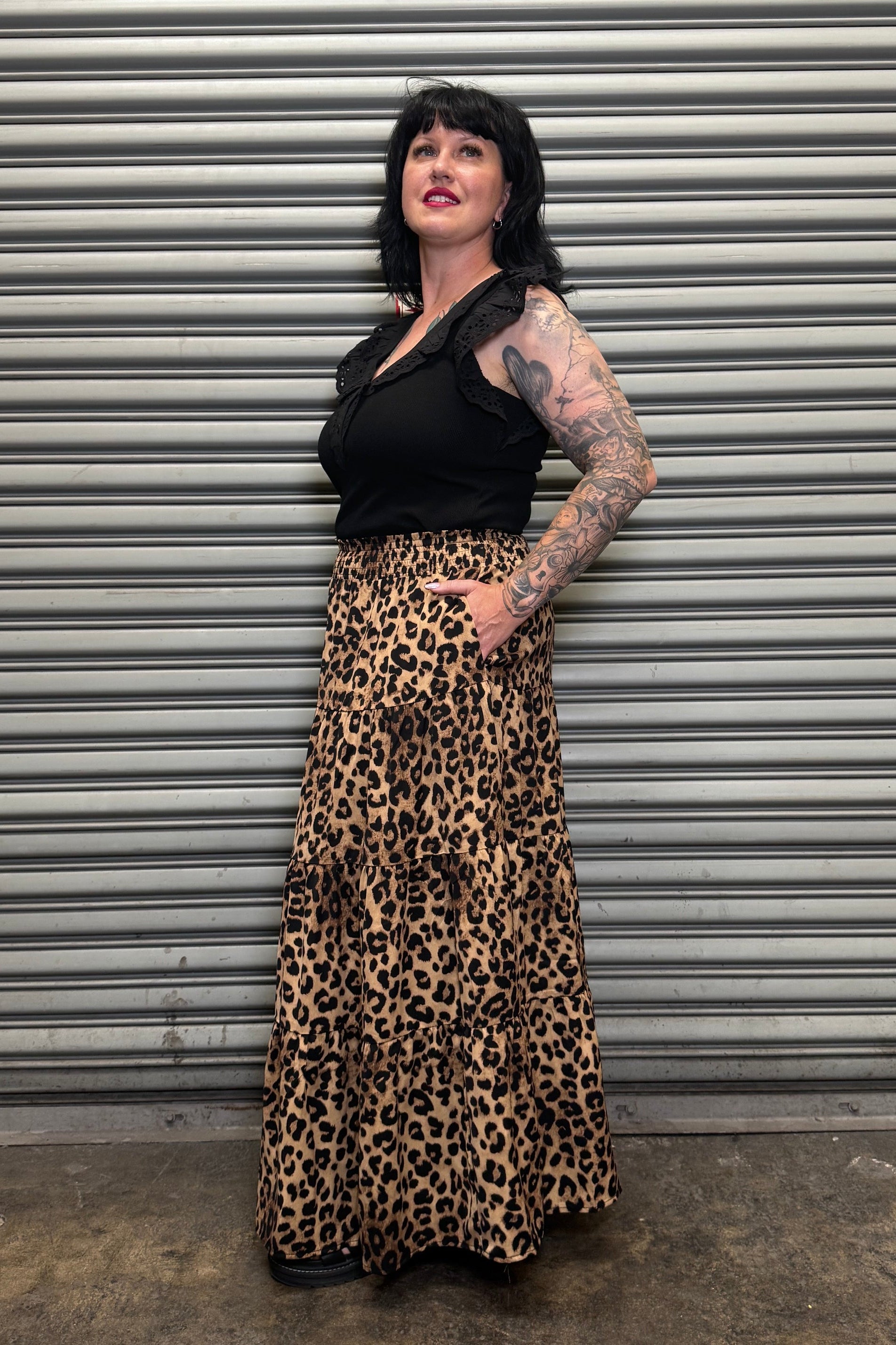 Side view of the Wild Heart leopard print tiered maxi skirt with pockets paired with a black ruffle sleeve top.