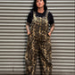 Women with black hair and tattoos standing in front of metal backdrop wearing leopard overalls.