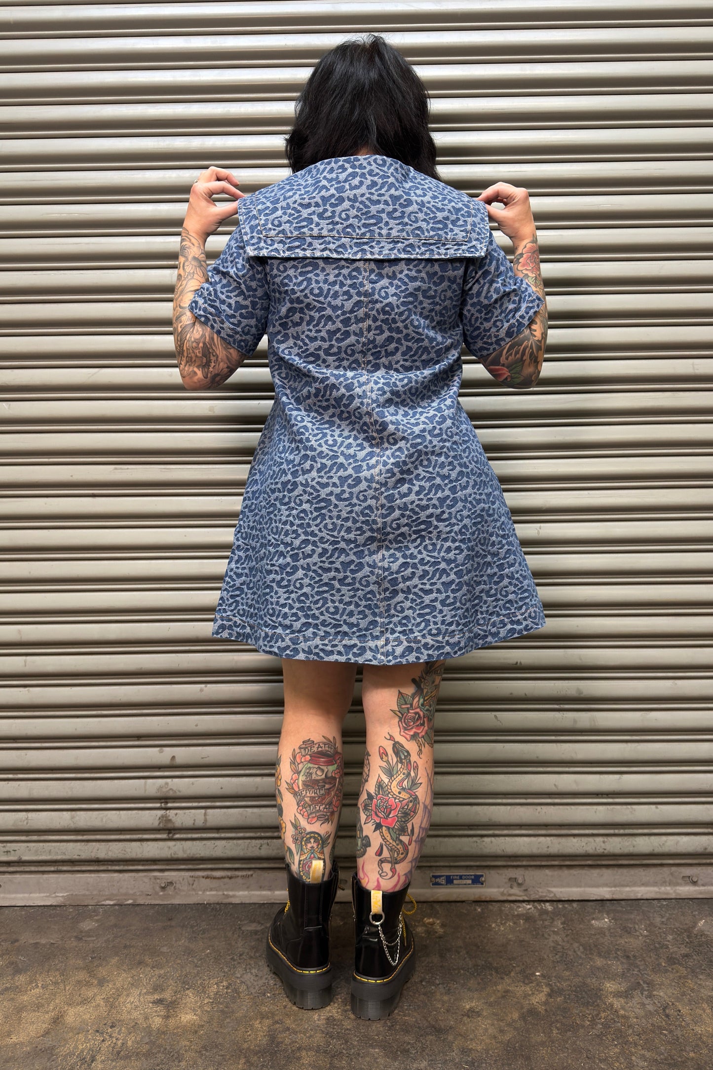 Person wearing a blue patterned dress standing in front of a metal shutter.