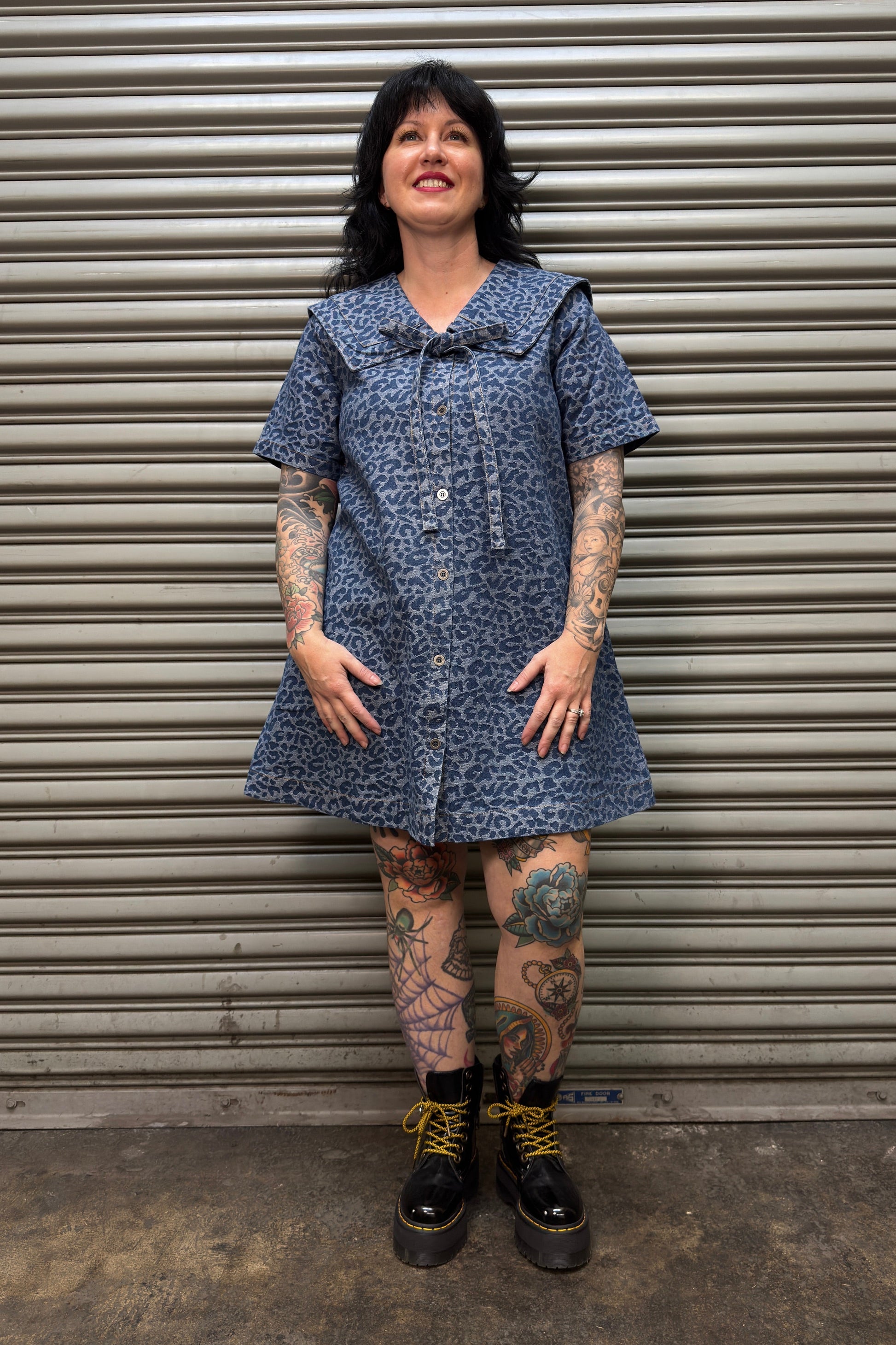 Person wearing a blue patterned dress standing in front of a metal shutter.